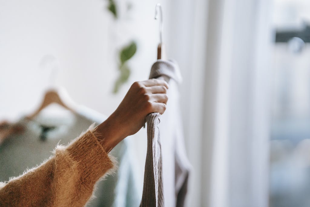 A woman choosing between garments hanging on a wooden hanger inside a cozy room.